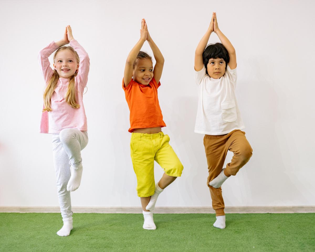 three children doing yoga and standing in tree pose